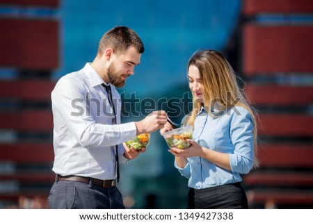 young businesswoman and businessman eating together salad in lunch box on outdoor. 