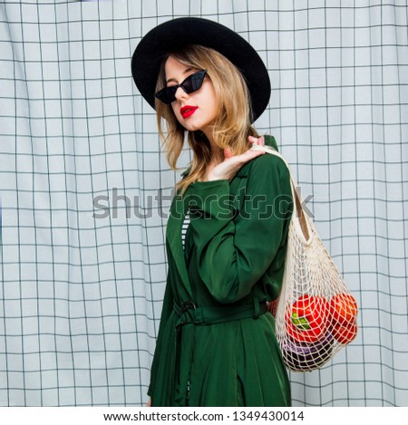 Young style woman in hat and green cloak in 90s style with net bag stay on checkered background