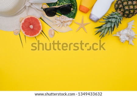 Beach flat lay accessories. Sun hat, towel, camera, cream, swimsuit, slippers, sunscreen bottle, exotic fruits, and seashells on a yellow background. Summer travel holiday concept