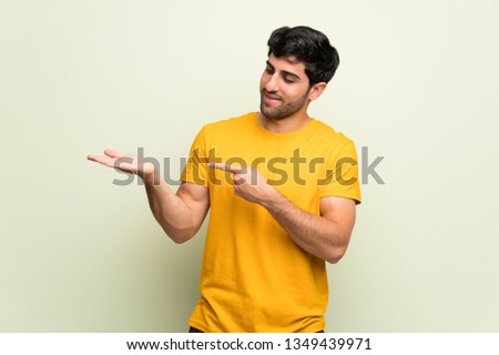 Young man over pink wall holding copyspace imaginary on the palm to insert an ad
