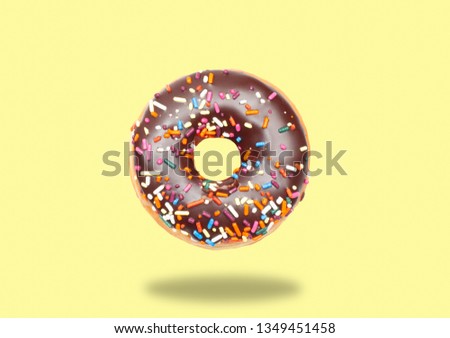 Chocolate donut with icing on pastel yellow background.