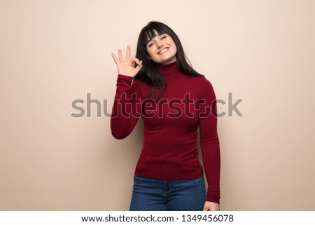Young woman with red turtleneck showing an ok sign with fingers