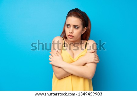 Young redhead woman over blue background freezing