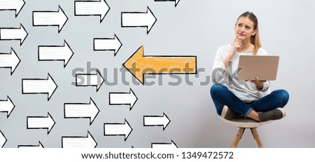 Arrow going in a opposite direction with young woman using her laptop on a grey background