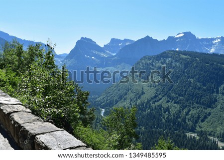 Landscape picture of a river winding through mountains in a green tree covered valley, under a clear blue sunny sky off of the Going-to-the-Sun Road in Glacier National Park in Montana.