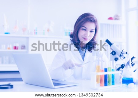 Asian female scientists use a tongs to pinches glass test tubes for her experiment result, colorful test tubes and notebook near her, she hope this experiment to find new experimental good results.
