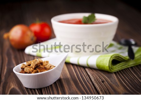 Fresh red tomato cream soup in white bowl. Dish and ingredients photography taken on old wooden table.