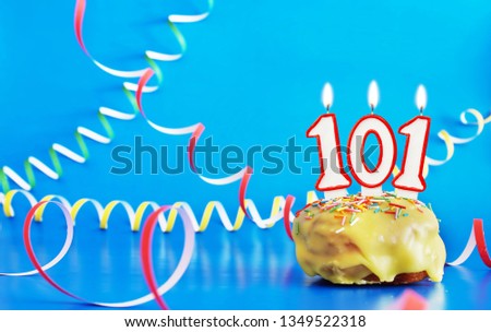 Birthday of one hundred and one years. Cupcake with white burning candle in the form of number 101. Vivid blue background with copy space
