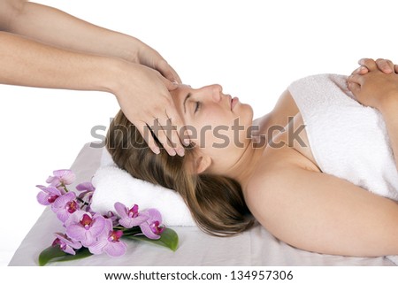 Spa therapy getting a head massage by technician masseuse for happy pretty young blonde woman, wrapped in towel while enjoying aroma therapy laying on massage table. In studio on white background.