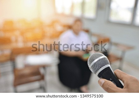 Hand holding microphone for interviewing, professional and educational concept of a microphone in selective focused image with blurred background of a person in an interview room