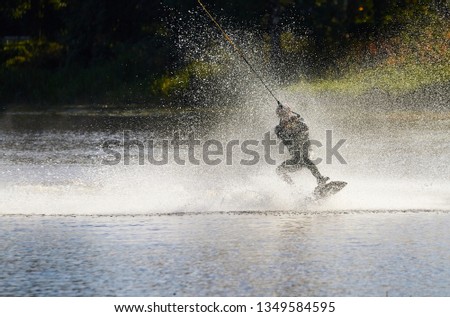Wakeboarder surfing across a lake with water splashing. This is an extreme sport.