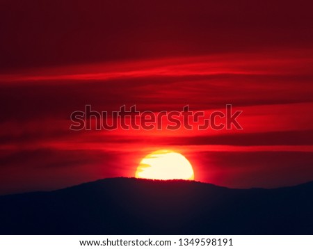 Tranquil autumn sun is rising from behind mountains, in a cold day with cloudy sky. Red perfect sun is lighting the sky with fire. Autumn sunrise landscape background.