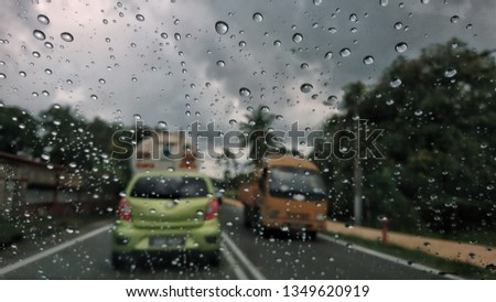 View of traffic on the street during a rain from the inside of a car through the windshield with drops of water. Image maybe sightly blur, noise or grain.