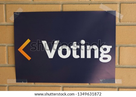 White text on blue background voting sign  on  cream brickwork with  a yellow and orange arrow 