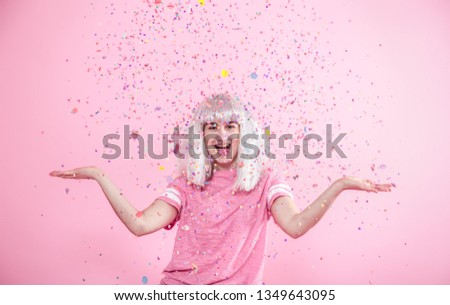 Funny Girl with silver hair gives a smile and emotion on pink background. Young woman or teen girl with confetti. Concept of holiday and party.