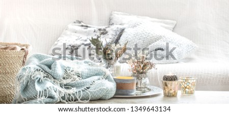 Home decorations in the interior. On the wooden background lies a turquoise blanket and wicker basket with a vase of flowers and candles. Concept of comfort