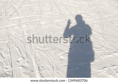 a photographer is taking a picture of his shadow and  waving with his hand on the snowed grownd. Winter season outdoors.  