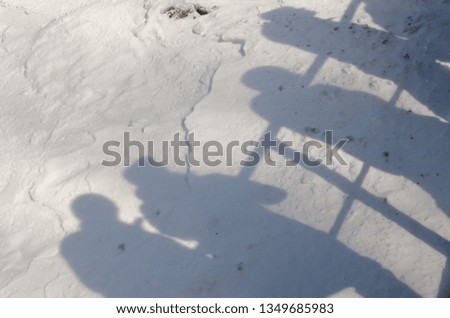 a photographer is taking a picture of his shadow and other people on the snowed grownd. Winter season outdoors.  