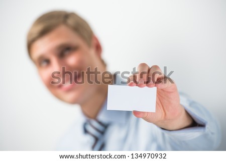 Happy smiling business man showing blank businesscard and dreaming, while leaning on wall at office