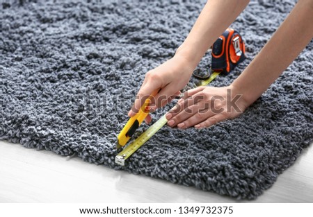 Woman with tape measure cutting carpet on floor Royalty-Free Stock Photo #1349732375