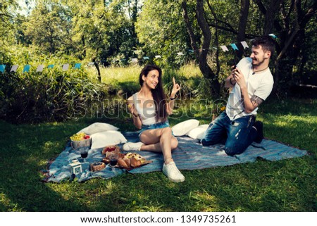 Young couple on a picnic in a city park sitting on a blanket He takes a picture of her Selective focus