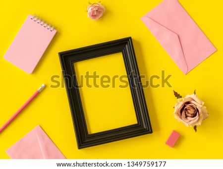 pastel space notebook and black picture frame with rose flower and pencil on yellow background