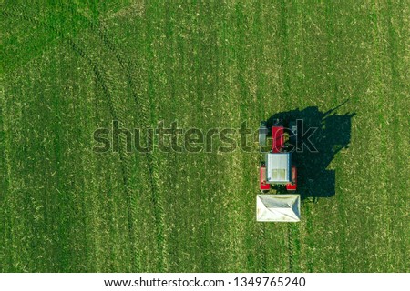 Agricultural tractor is fertilizing wheat crop field with NPK fertilizers, aerial view from drone pov