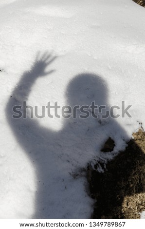 a photographer is taking a picture of his shadow and  waving with a hand on the snowed grownd. Winter season outdoors.  
