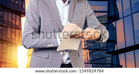 A man holds documents in his hand and makes a signature on the background of a skyscraper. The concept of business success.