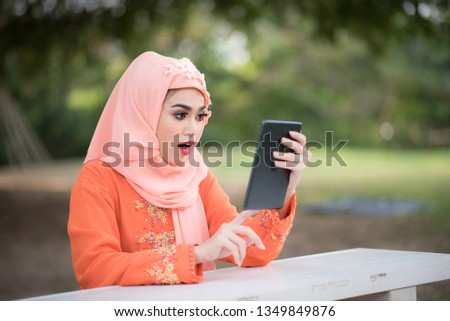 Asia beautiful muslim women sitting in the park and looking holding a tablet.