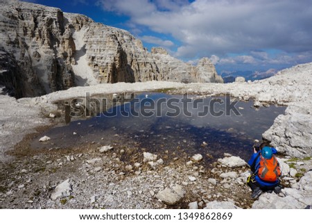 Young male hiker with backpack taking pictures of a lake in Sella, Dolomiti mountains, Italy