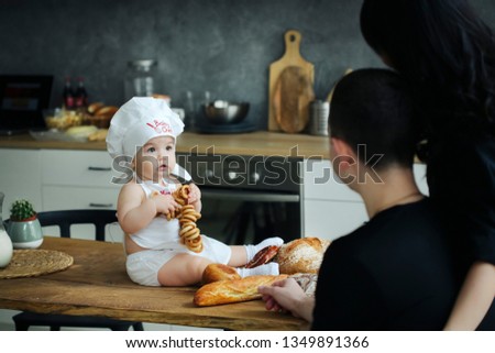 Parents and their newborn daughter in a white apron are busy preparing bread and pizza at the bakery table. Black clothes style.Nutrition concept. Making pizza.Organic healthy baking food concept