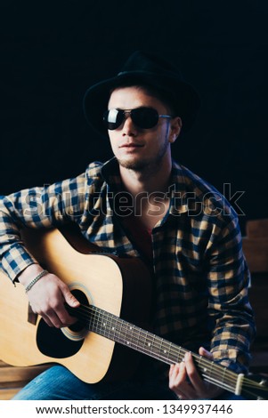 cool man in hat and glasses with guitar on black background