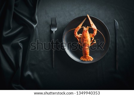 Boiled lobster in a black plate on a black background, top view. Boiled big red fresh crawfish in black plate with black tableware Royalty-Free Stock Photo #1349940353