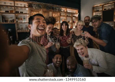 Diverse group of young friends laughing and talking selfies together during a fun night in a bar