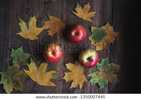 Ripe apples and autumn maple leaves on wooden background.