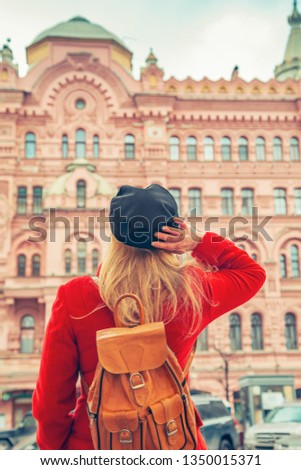 Woman in a red coat and a black cap looks at a beautiful pink house. Back view. Saint-Petersburg, Russia - 15 March, 2019. 