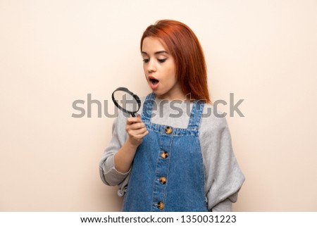 Young redhead woman over isolated background holding a magnifying glass