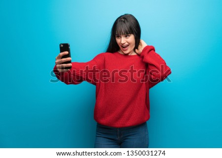 Woman with red sweater over blue wall making a selfie
