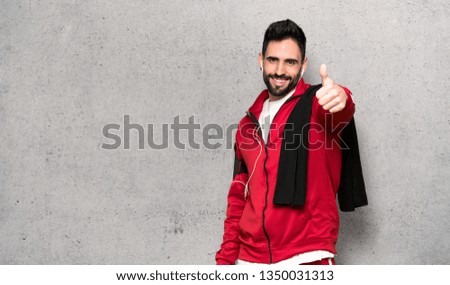 Handsome sportman giving a thumbs up gesture because something good has happened over textured wall