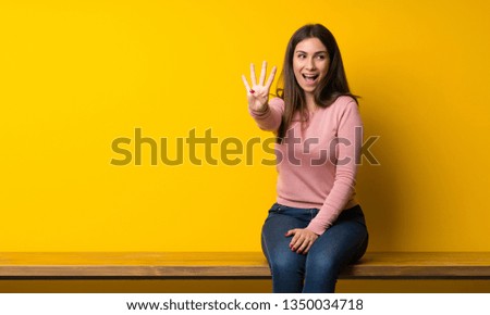 Young woman sitting on table happy and counting four with fingers