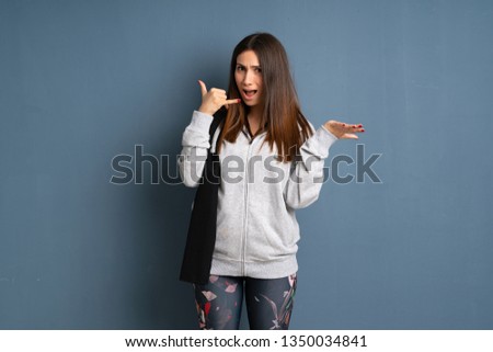 Young sport woman making phone gesture and doubting