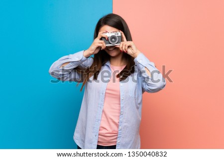 Young woman over pink and blue wall holding a camera