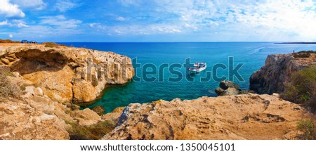 Image with panoramic view of a bay near Cape Greco, Cyprus. Rock coastline near deep green transparent azure water, one white boat, cars. Amazing cloudscape. Warm day in fall