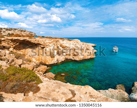 View of a bay near Cape Greco, Cyprus. Rock coastline near deep green transparent azure water, one white boat, two cars. Amazing cloudscape. Warm day in fall
