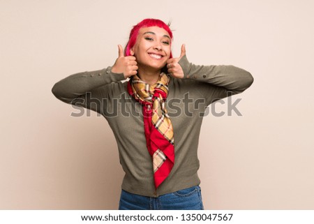 Young woman with pink hair over yellow wall with thumbs up gesture and smiling
