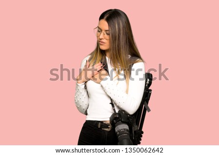 Young photographer woman having a pain in the heart on isolated pink background