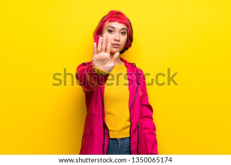Young woman with pink hair over yellow wall making stop gesture