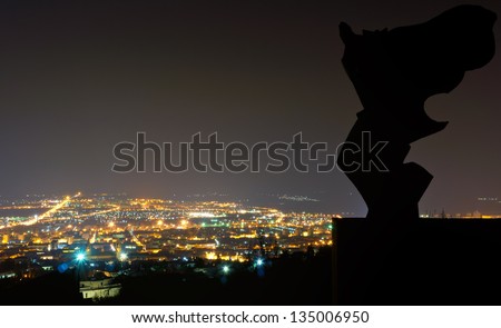 Angel over the City/Silhouette from an angel statue, the City of Pecs in the background at night time.This Photo was taken from the Mecsek mountain in Hungary.