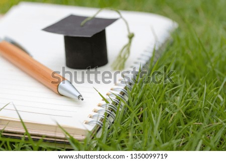 Learning and Education concept. miniature  Square Academic Cap and pen in white notebook and green grass. Graduation.